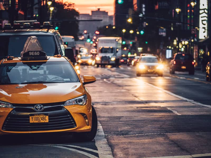 yellow taxi cab parked on the side of the road in new york city with traffic in the background