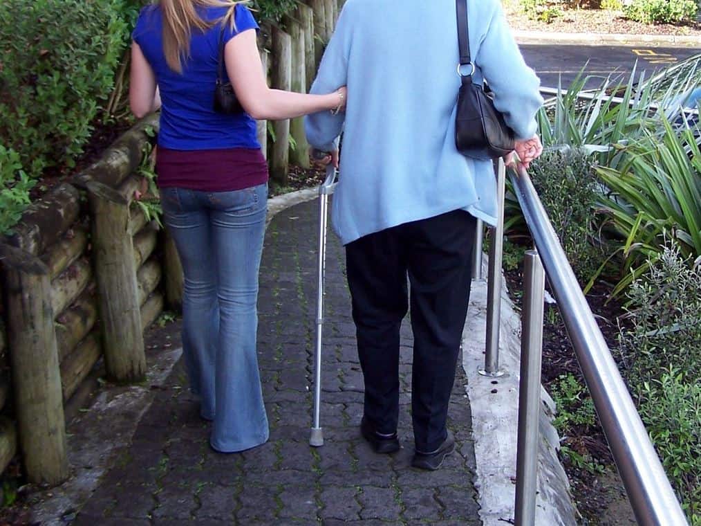 woman assisting an elderly woman walking with a can