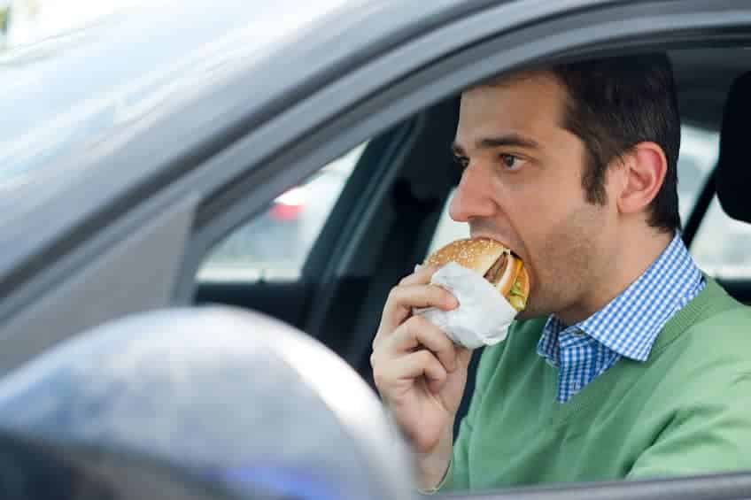man eating a burger while driving a car