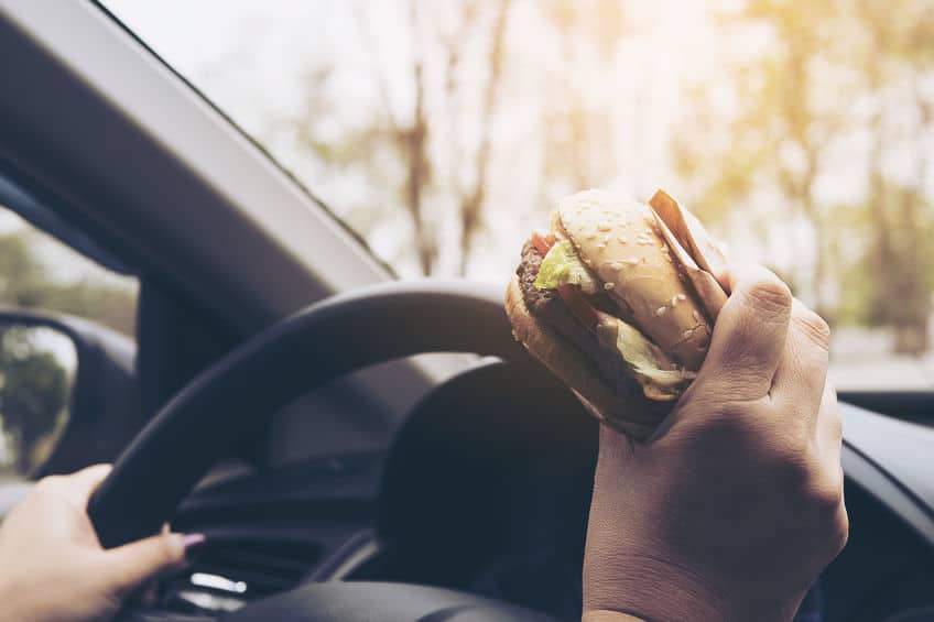 person driving a car while eating a burger