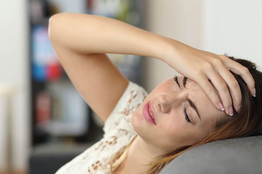 woman on a couch with a headache from a concussion and hand on her forehead