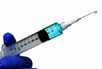 hand holding a syringe with fluid dripping off the needle