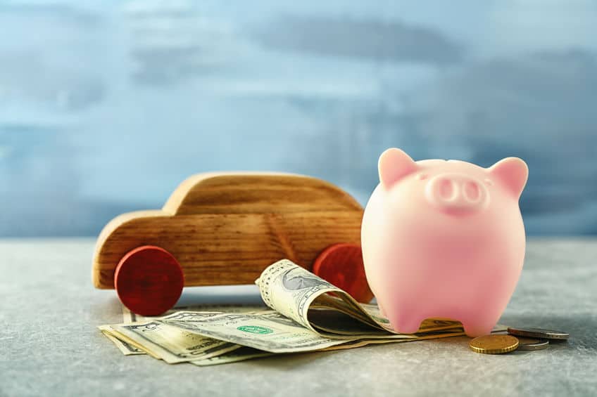 piggy bank with money under it and a wooden car on the table to demonstrate car insurance