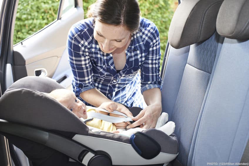 woman putting a baby into it's car seat facing the rear in a car