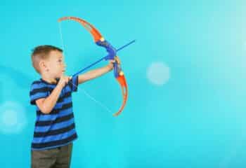 boy shooting a toy bow and arrow against a blue background