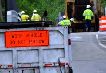 close up on a sign saying work vehicle do not follow with construction workers and equipment in the background