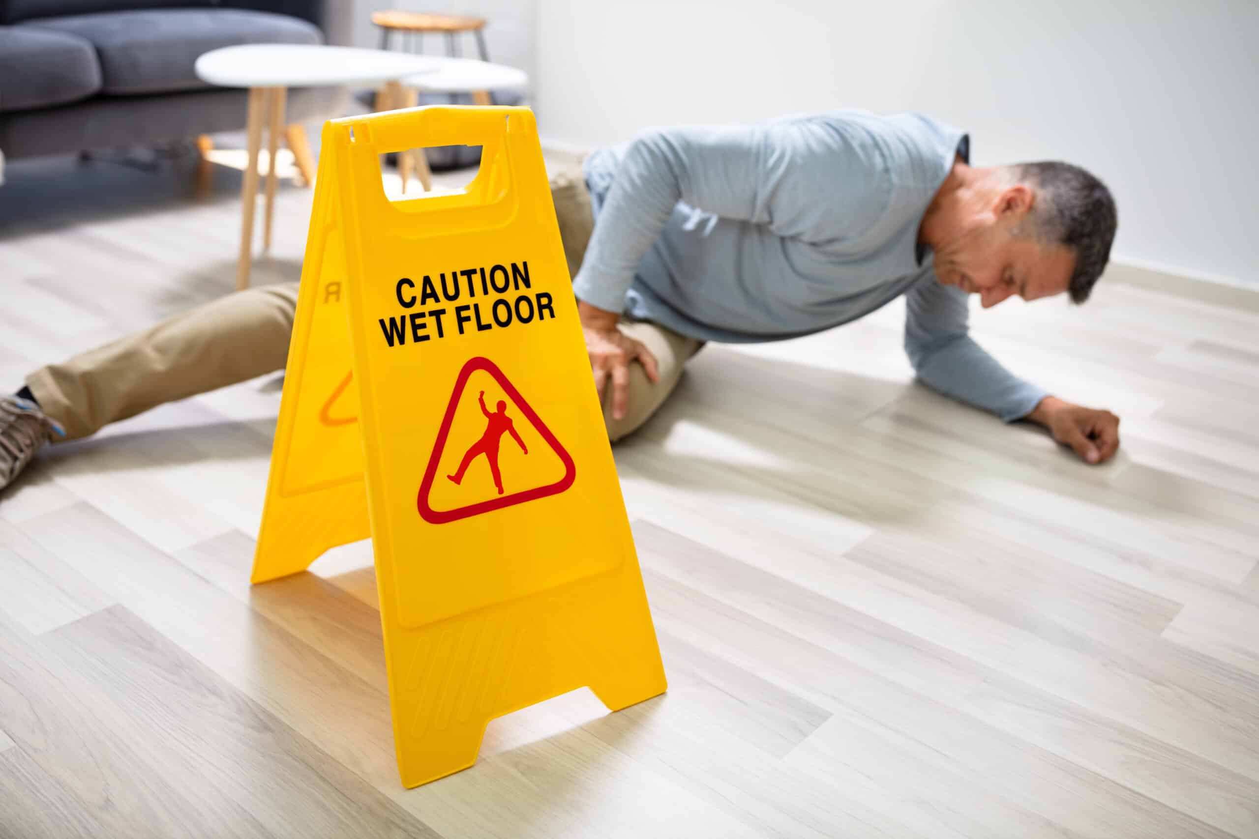 man falling on ground next to wet floor sign
